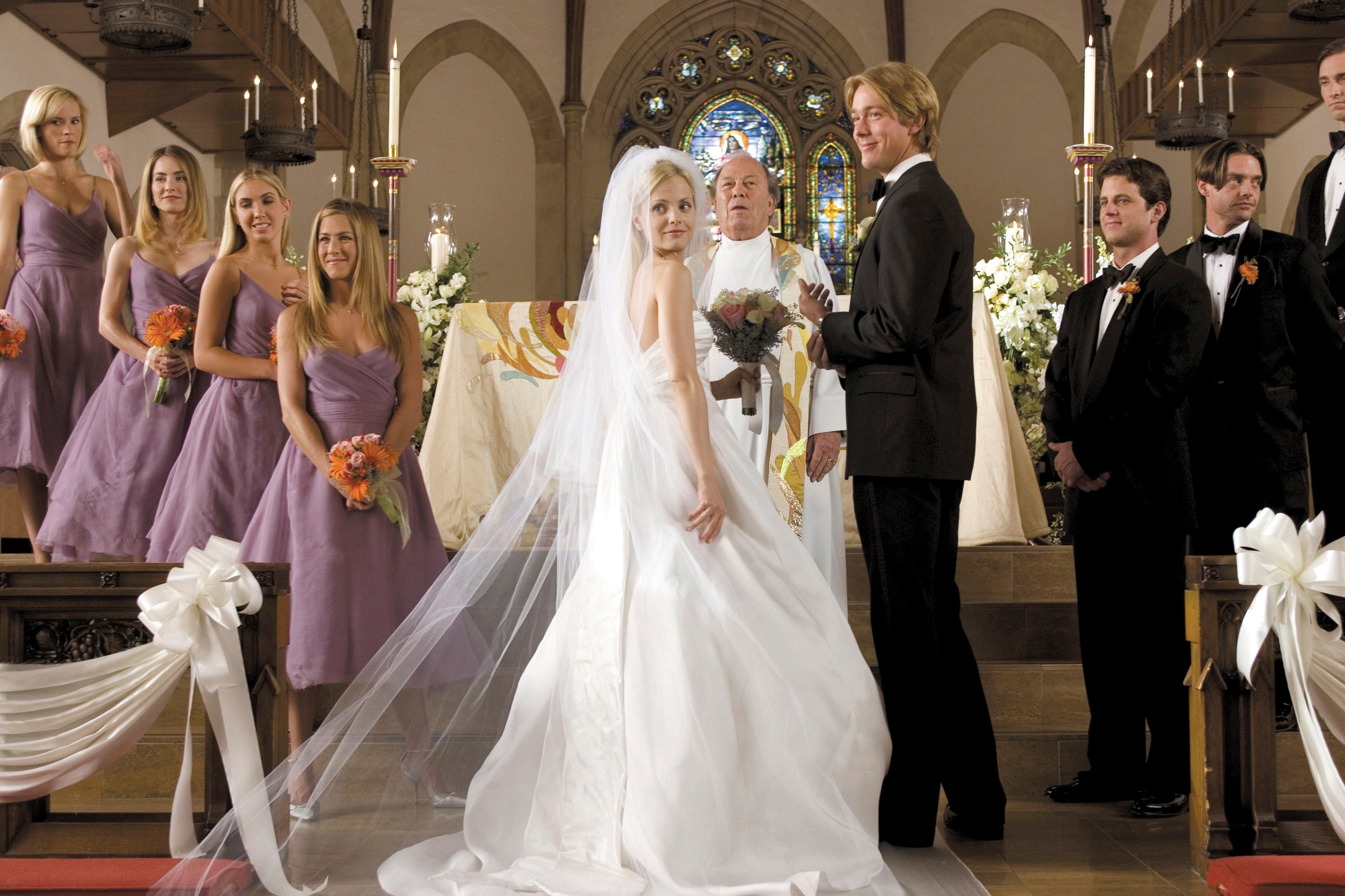 Bridal party in elegant attire stands at the altar during a wedding ceremony in a church, with the bride and groom exchanging vows