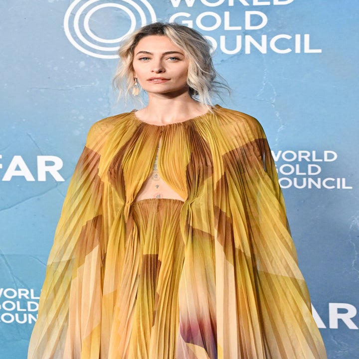 Person in pleated gown with sheer details at event, standing against a backdrop with "World Gold Council" logo and text