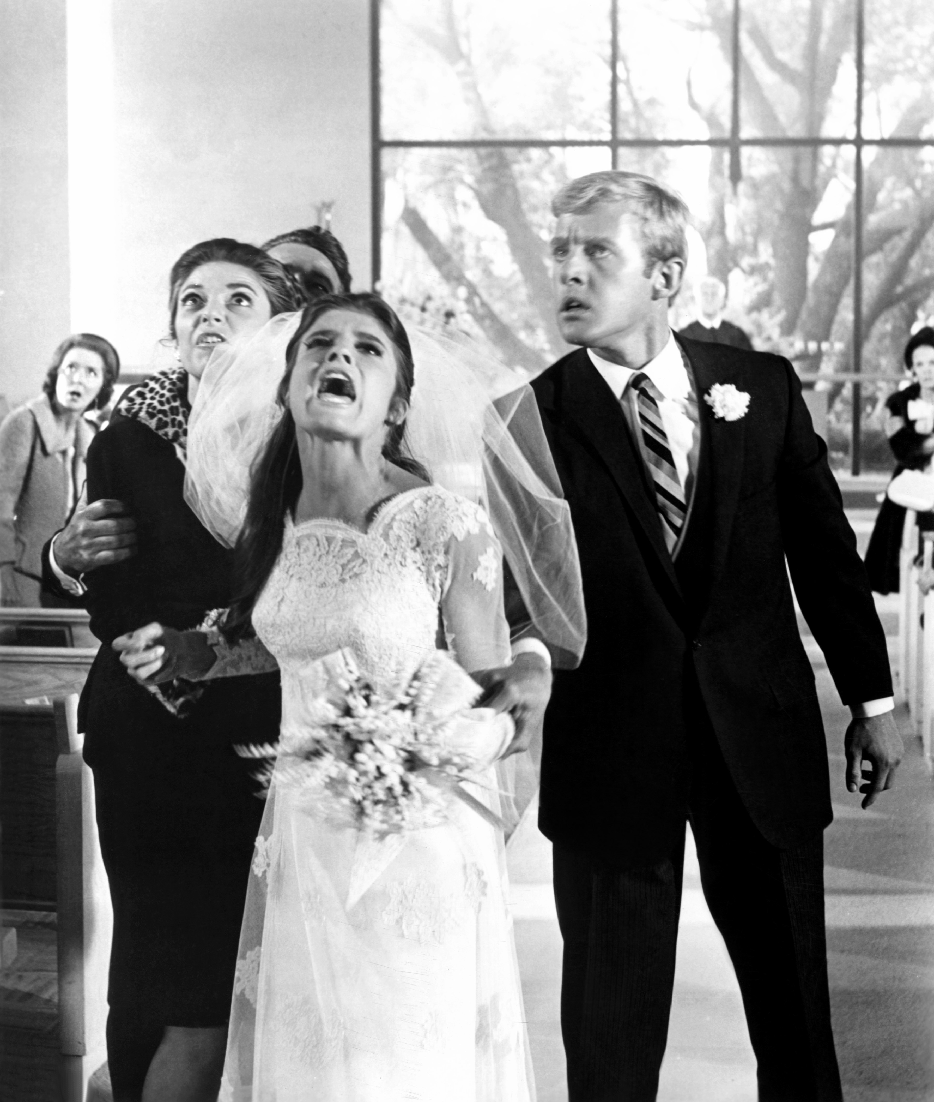 Bride in a lace gown appears upset, holding flowers on a dramatic wedding day scene indoors. Other individuals express concern around her