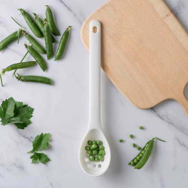 White spoon with peas, parsley, and a cutting committee  connected  a marble surface. Ideal for cooking oregon  room  mentation  articles