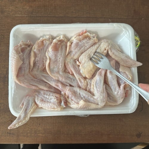肉のトレイにフォークが差し込まれた生の鶏の手羽先が並べられています。