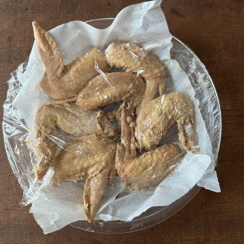 お皿にラップされた数枚の鶏の手羽先。