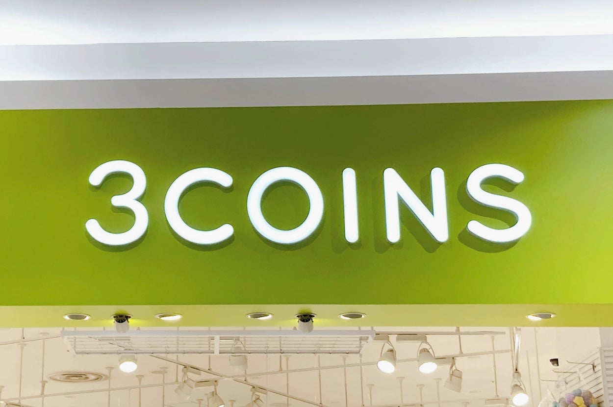 店舗の看板に「3COINS」と書かれた明るい店内の入口。販売アイテムのヒントが看板に示されている。