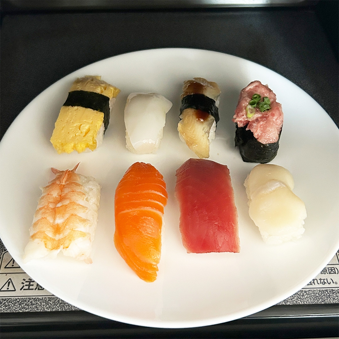 お皿に8種類の寿司が並んでいます。玉子、イカ、マグロ、サーモンなどがあり、さまざまなネタが楽しめます。
