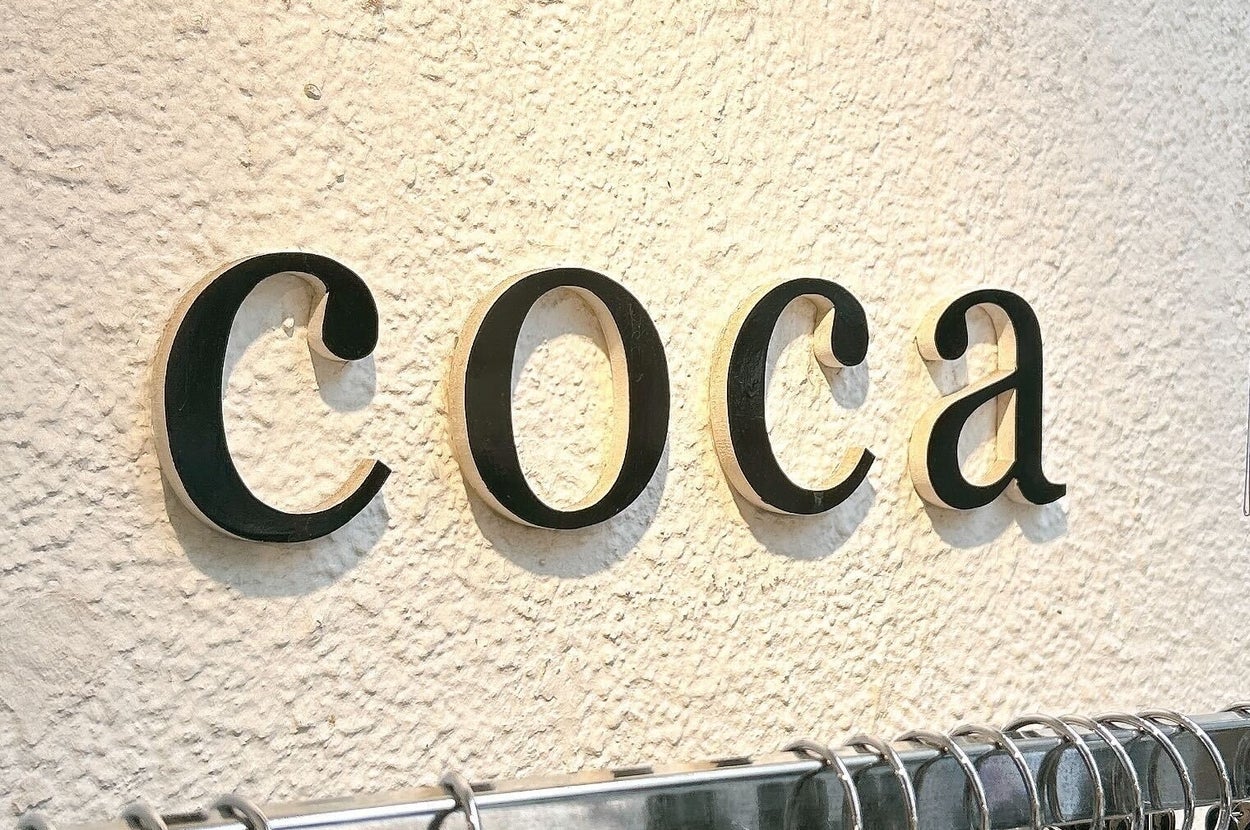 「coca」と書かれた壁面の上に洋服が並んでいる。