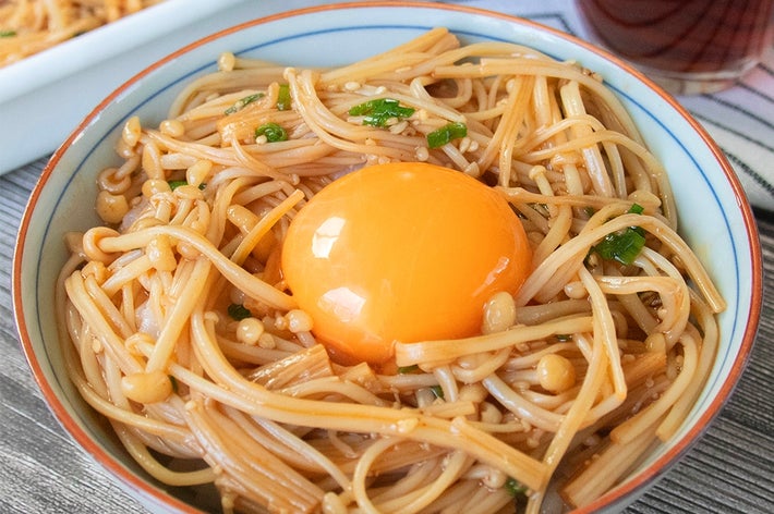 器に盛られた韓国風えのき漬けと卵黄がトッピングされた料理。横には飲み物がある。
