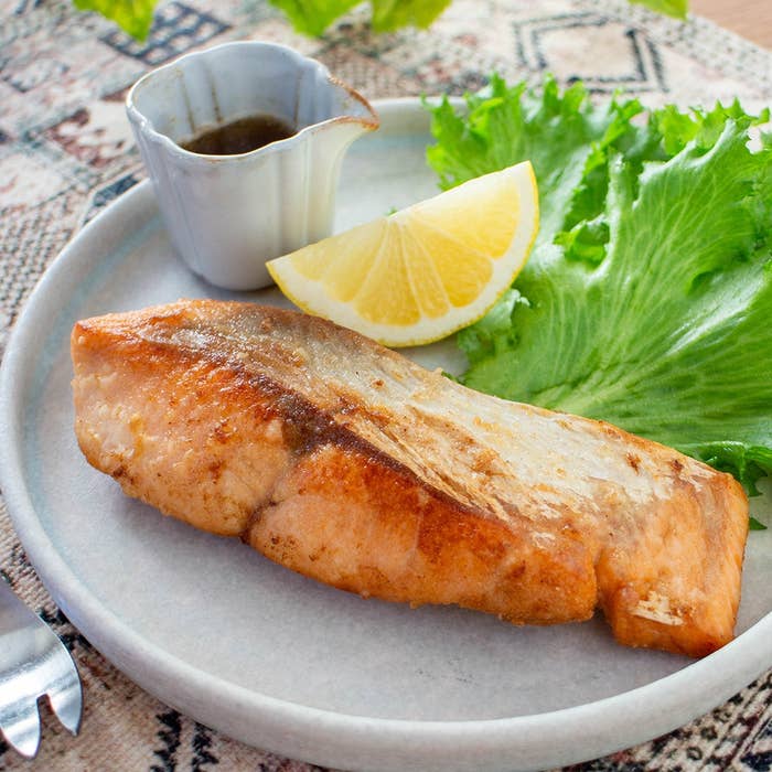 皿に乗った焼き鮭、レタス、レモン、タレの入った小さなカップが添えられている。