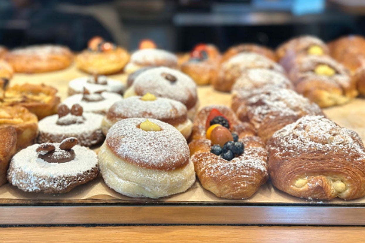 Assorted pastries displayed behind a glass counter, including donuts, croissants, and danishes with fruit toppings