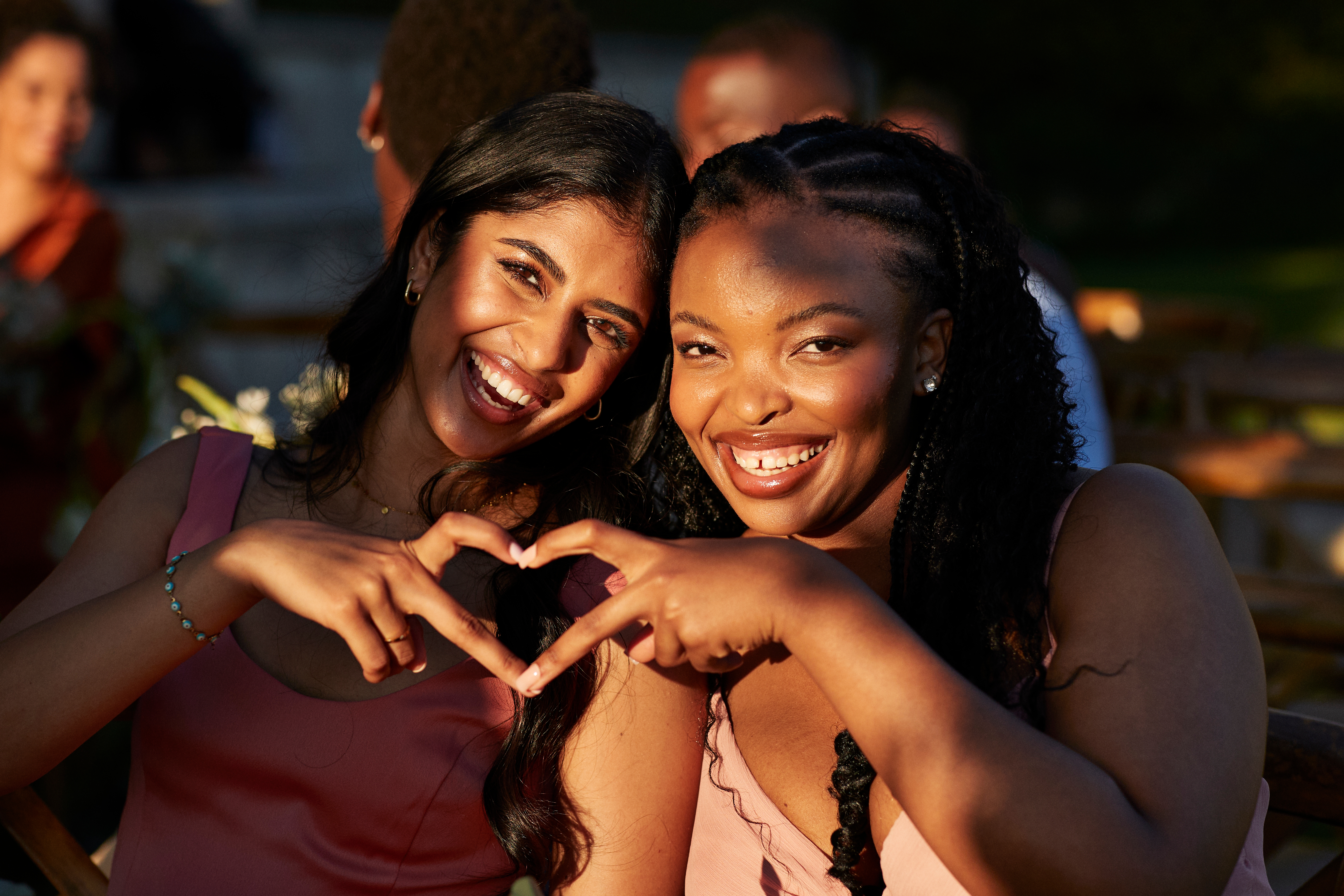 To personer som smiler til et utendørs arrangement, og danner en hjerteform med hendene