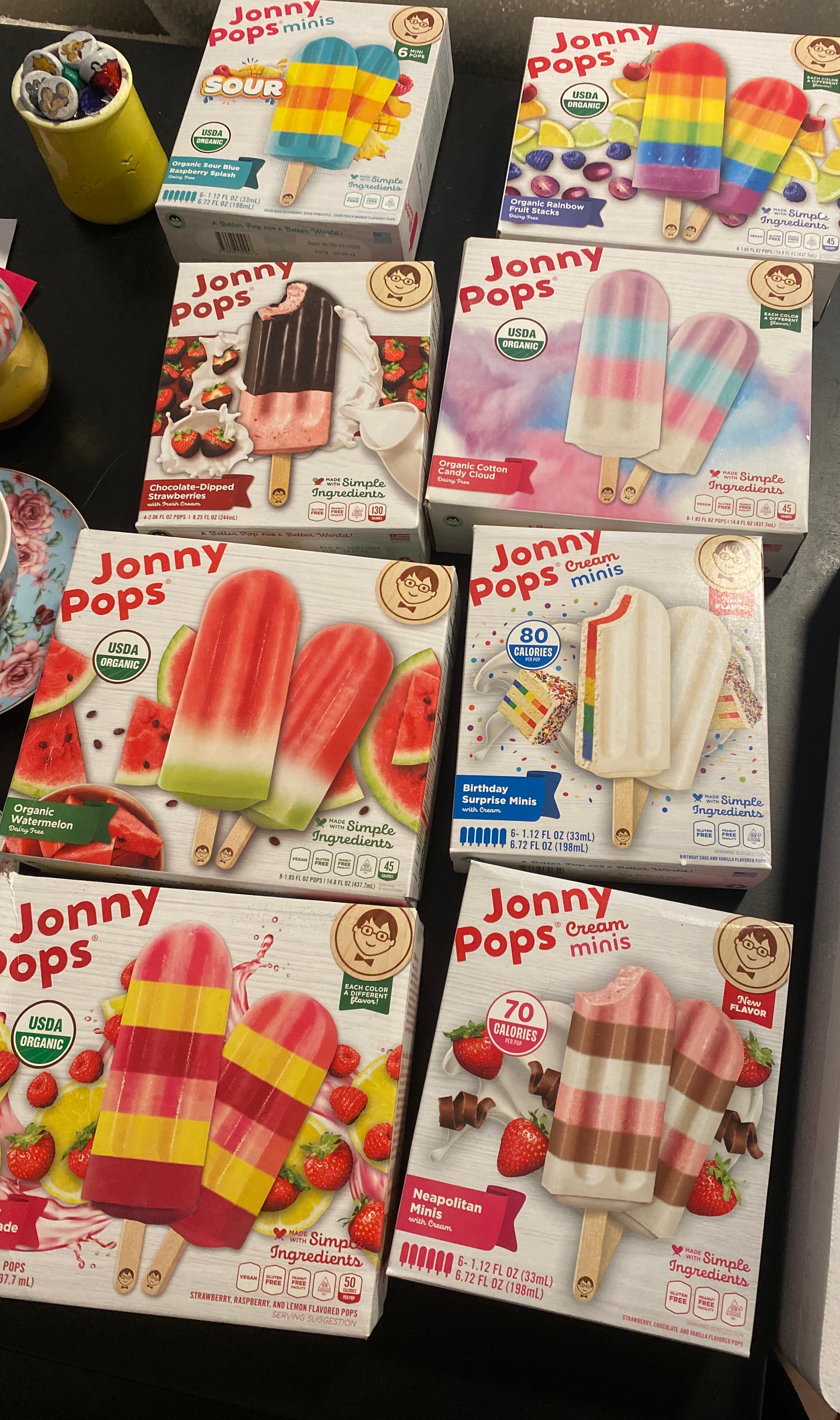Boxes of various JonnyPops frozen treats, including flavors like rainbow, watermelon, Neapolitan, and fruit bars, arranged on a table