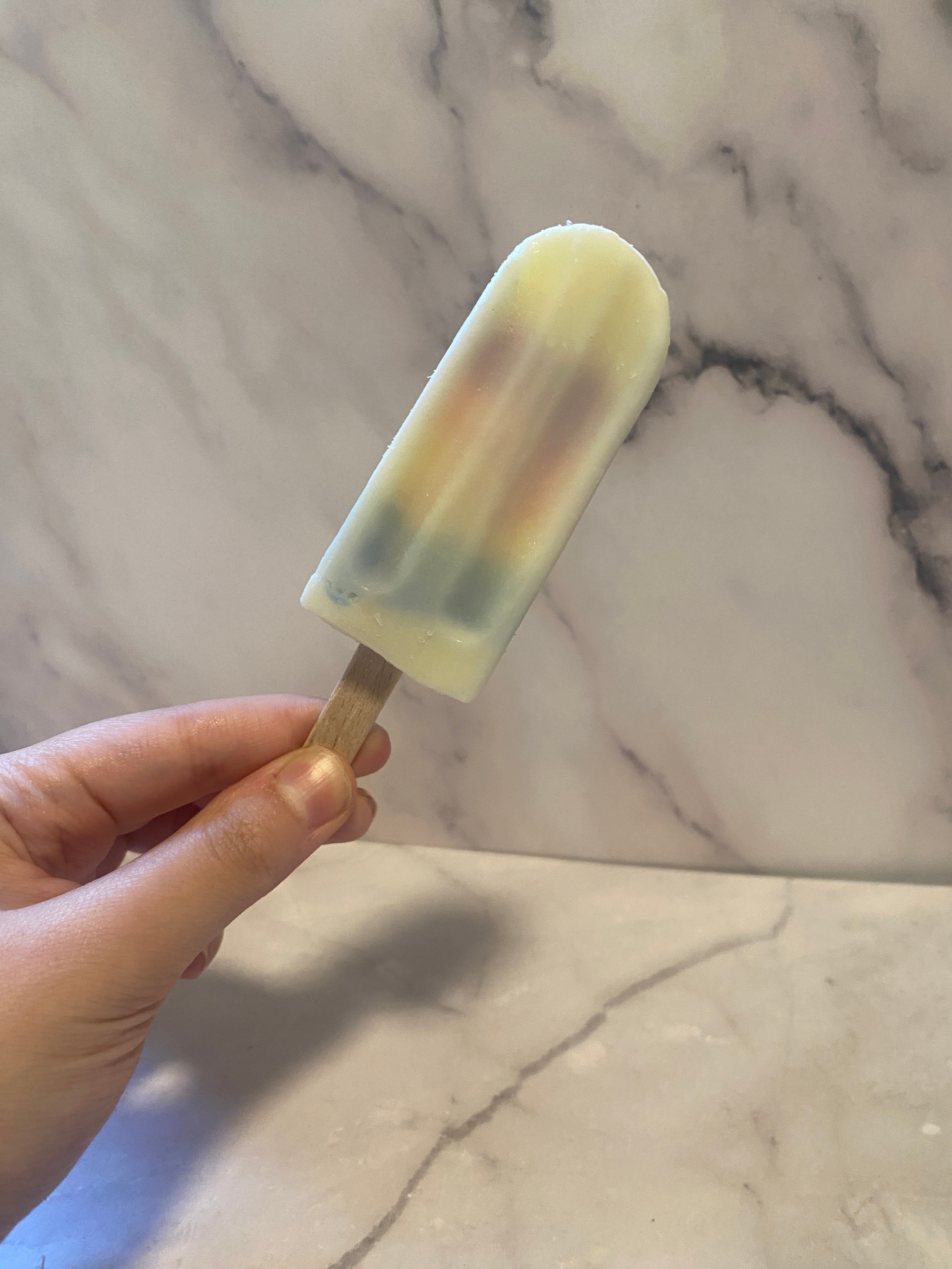 Person holds a marbled popsicle in front of a marble-patterned backdrop