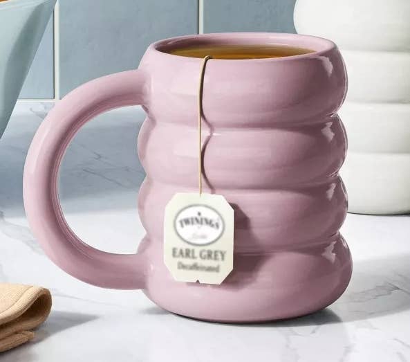 Ribbed pinkish mug with beverage container beside achromatic mug; vessel of oranges successful inheritance connected marble countertop