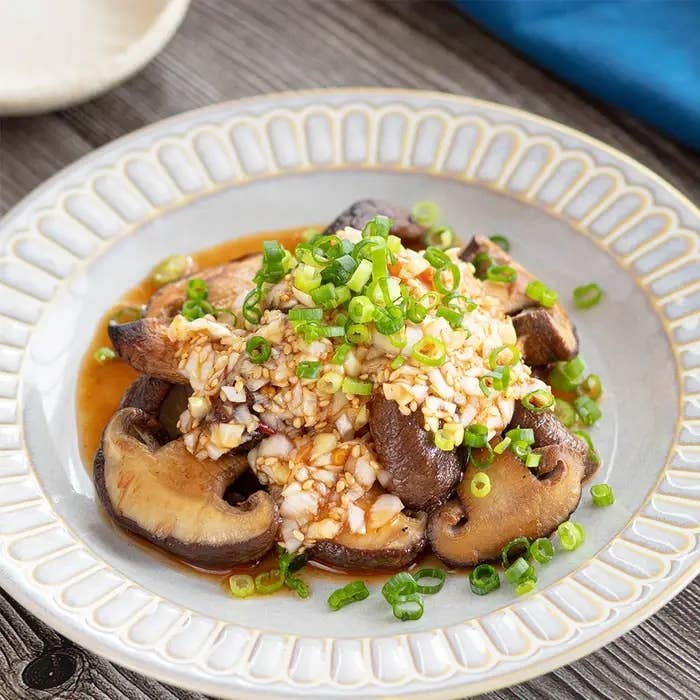 皿に盛られたガーリックソースがかかったシイタケ料理。ネギがトッピングされています。