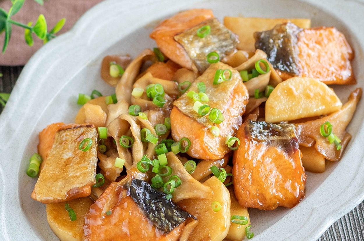鮭ときのことじゃがいもの炒め物が白い皿に盛られている料理。青ねぎが上に振りかけられています。