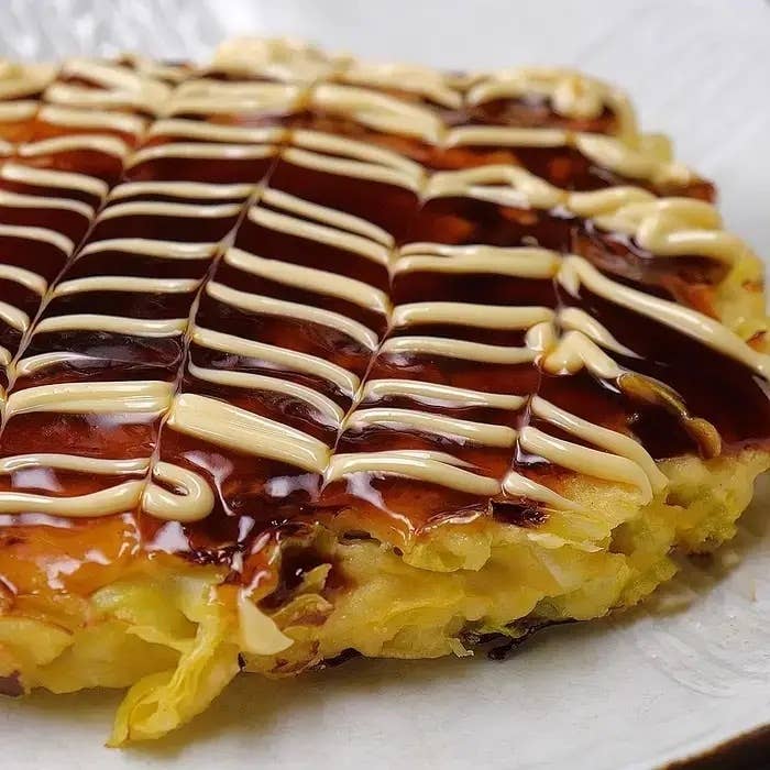 お好み焼きにソースとマヨネーズが美しくかけられているクローズアップ画像。