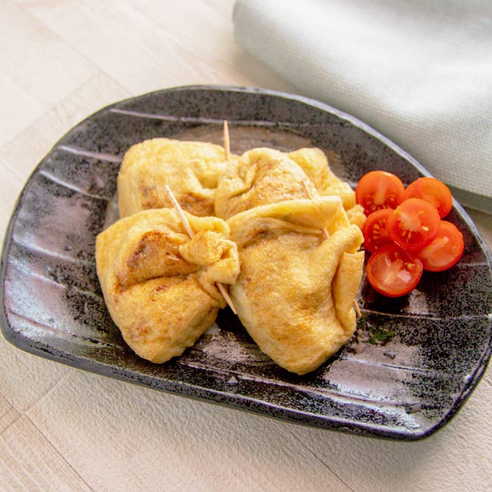 納豆きゅうりの油揚げ焼き。お皿に串で留めた油揚げが4つとミニトマトのカットが添えられている。
