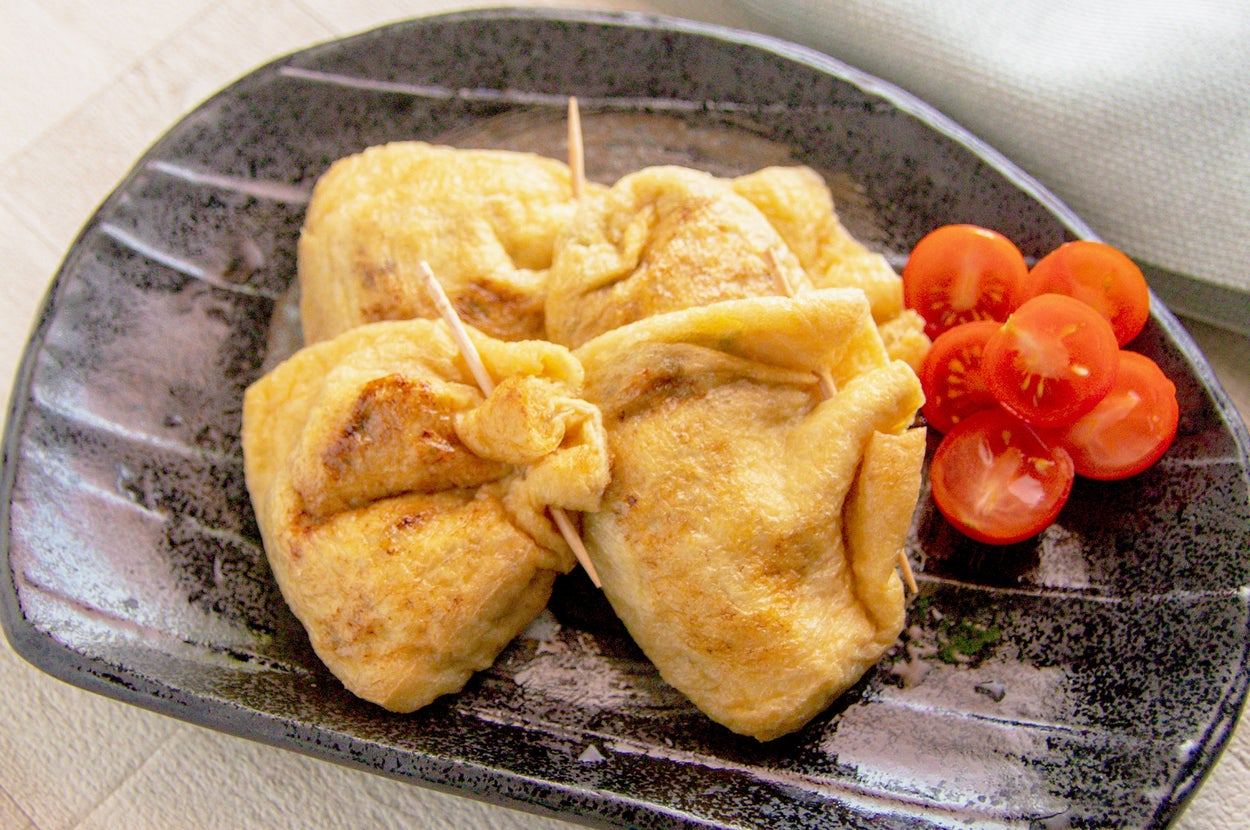皿に盛られた3つの巾着型の料理とチェリートマトの付け合わせ。