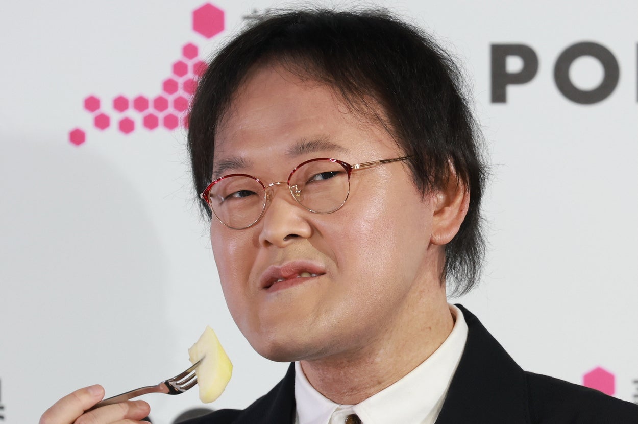 日本の男性がイベントでフォークを手にしながら、品のあるスーツスタイルでポーズをとっている。