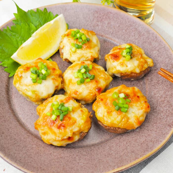 皿にのった6つのチーズ焼きしいたけ。ネギがトッピングされ、横にレモンのくし切りが添えられている。