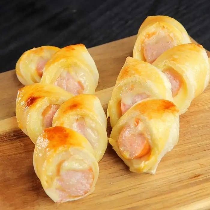 焼き色のついた小さなソーセージロールが木の板の上に並んでいます。