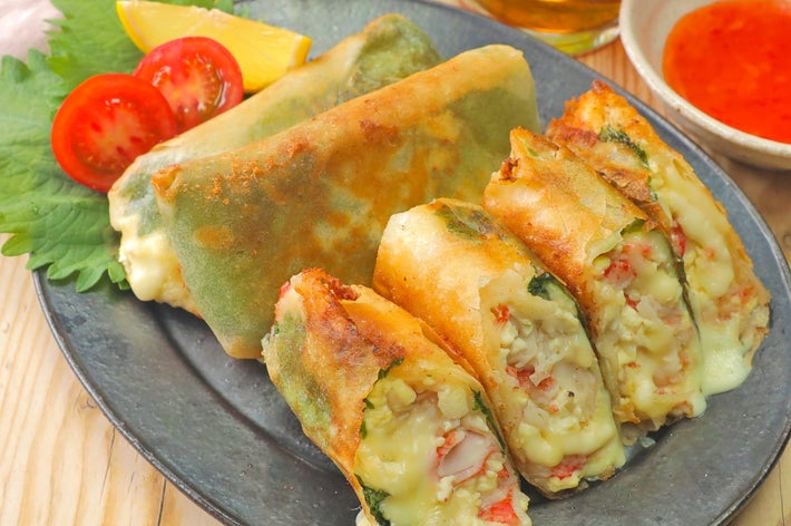 春巻きが盛り付けられたプレート。中身は野菜やチーズが見える。サイドにトマトとレモンが添えられている。