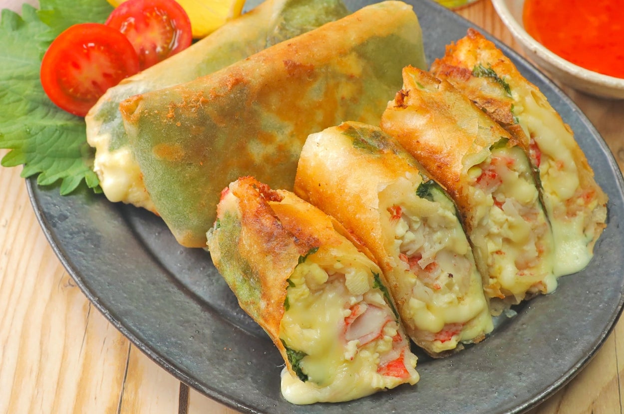 春巻きが盛り付けられたプレート。中身は野菜やチーズが見える。サイドにトマトとレモンが添えられている。