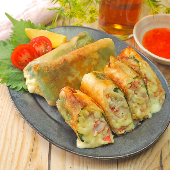 春巻きが盛り付けられたプレート。中身は野菜やチーズが見える。サイドにトマトとレモンが添えられている。