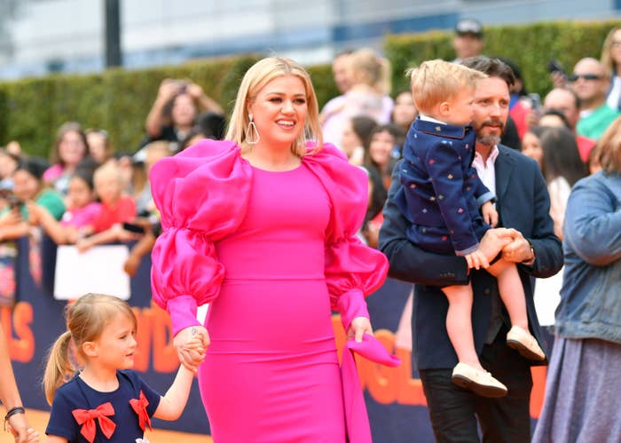 A pistillate successful a bold formal with voluminous sleeves attends an lawsuit with 2 children and a man, surrounded by a crowd