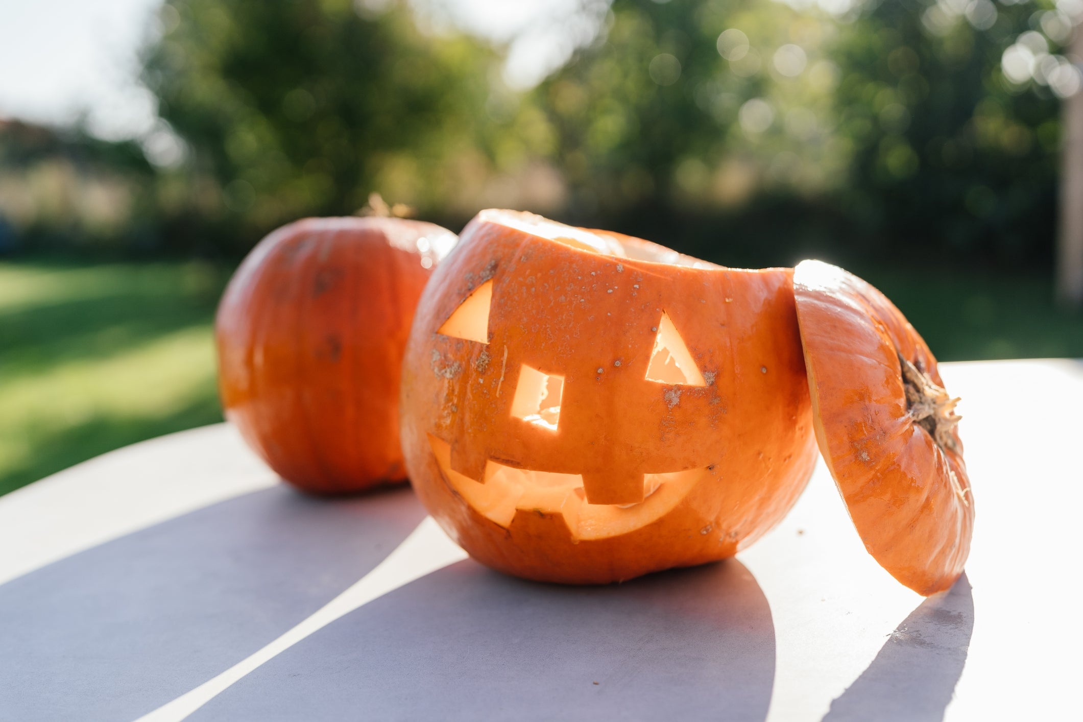 Carved jack-o'-lanterns on a table outdoors, one with a tilted lid, creating a playful expression