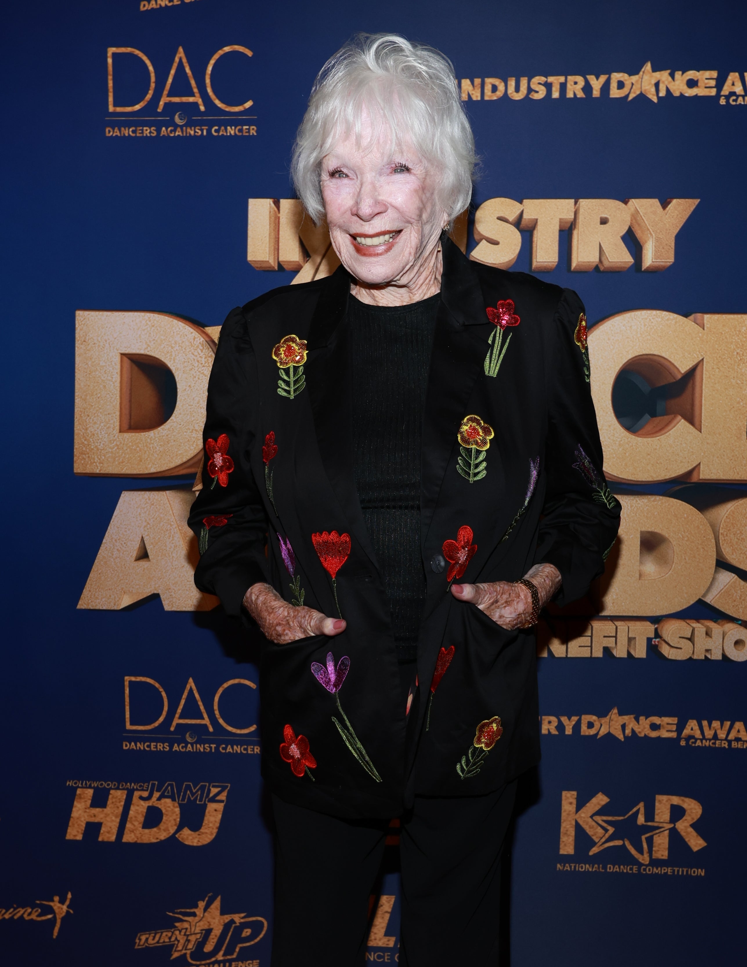 Shirley MacLaine smiles on the red carpet in a black suit with colorful floral embroidery at the Industry Dance Awards
