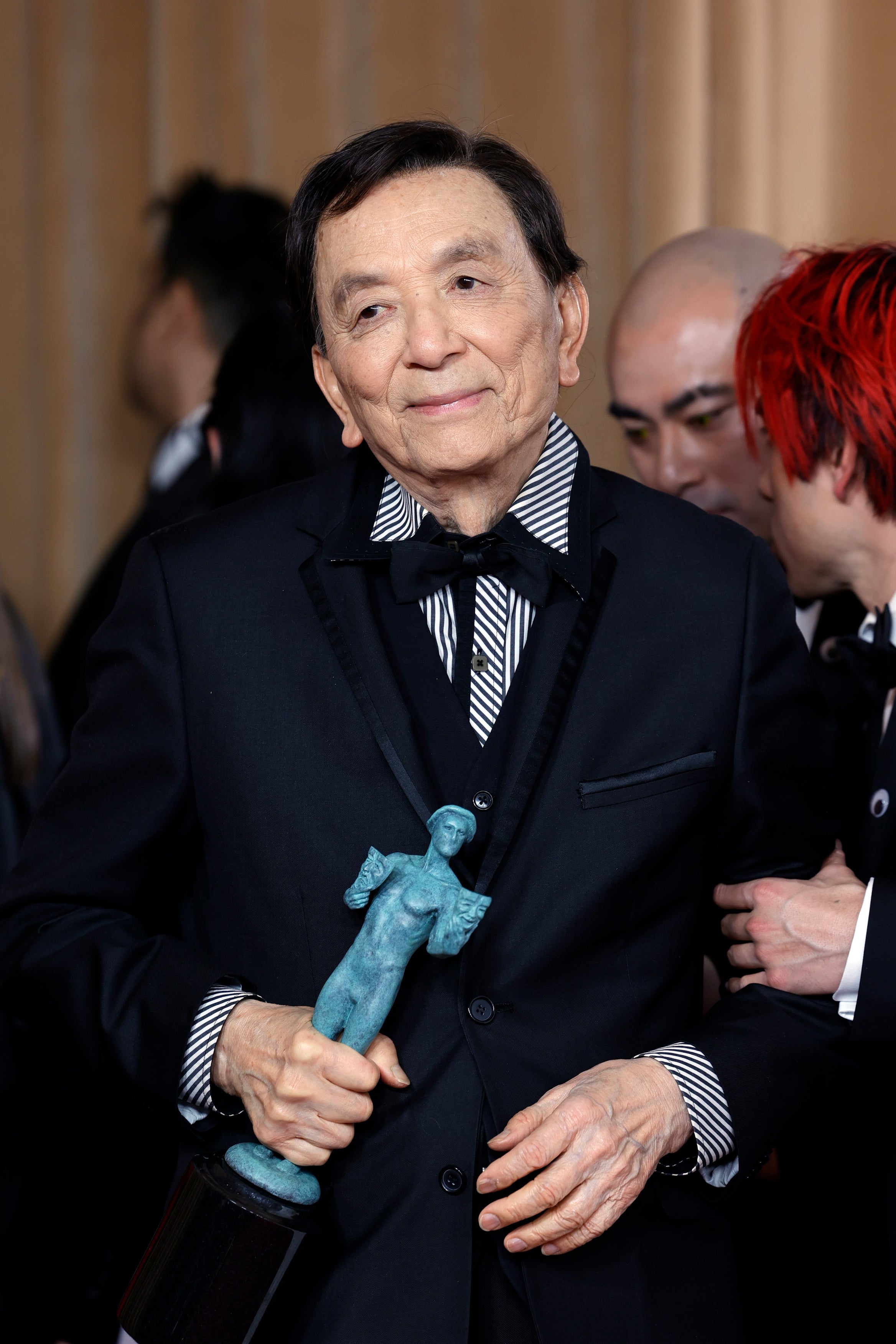 Person in formal suit holds an award statue, standing among others