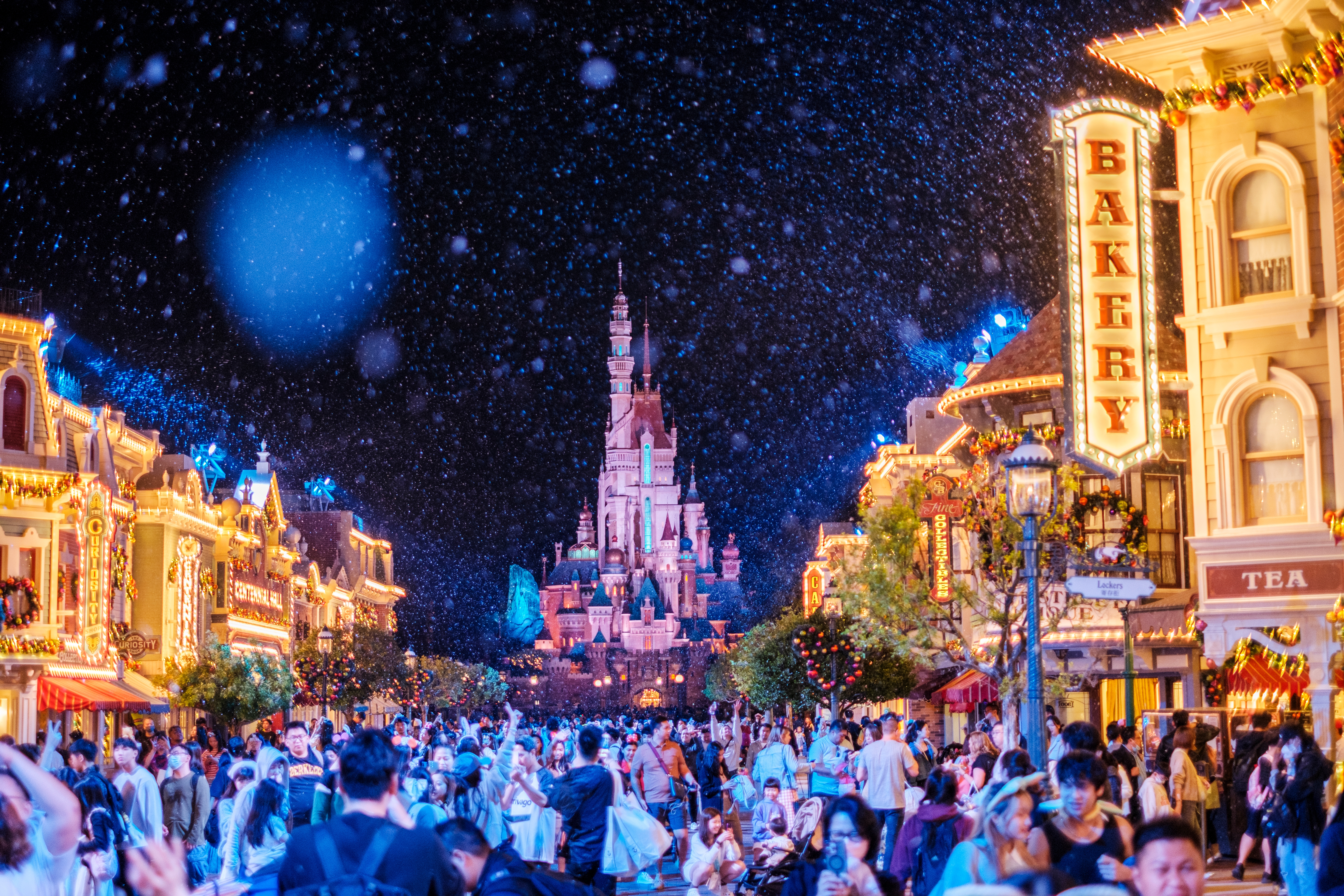 Et yrende publikum nyter en festlig natt på Disneyland, med et slott i bakgrunnen og snølignende effekter som gir en magisk atmosfære