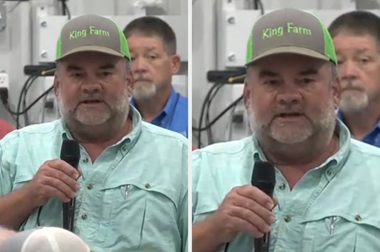 A man wearing a "King Farm" cap speaks into a microphone at an indoor event, with several people in the background