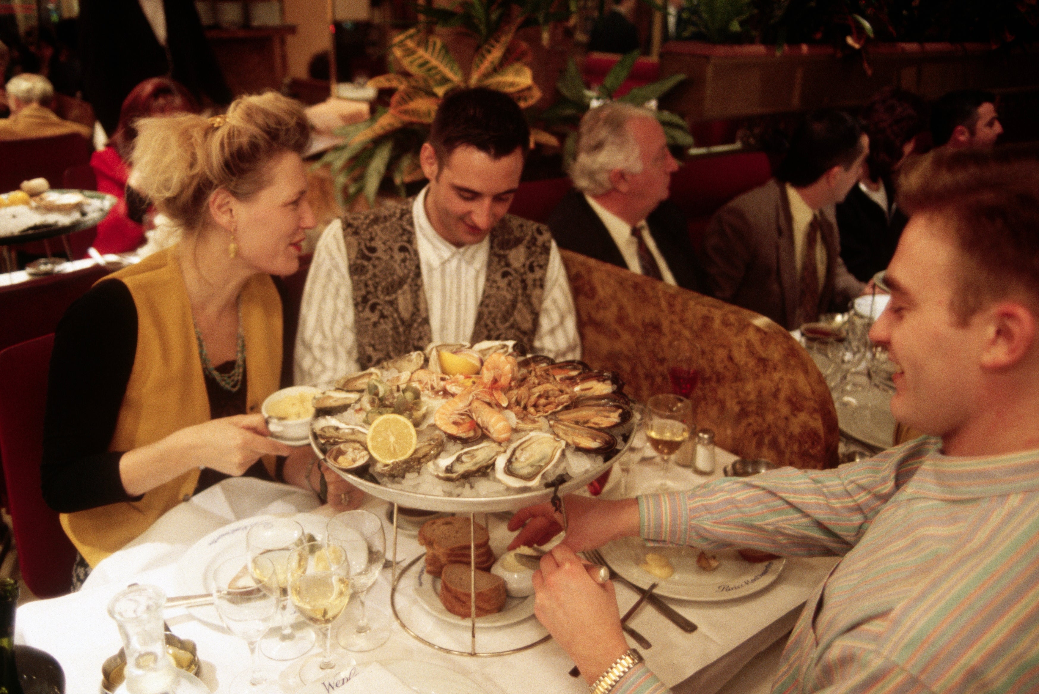 Gruppe som nyter en sjømatfat på en yrende restaurant, med østers og sitron på skjermen. Diners er engasjert i livlig samtale