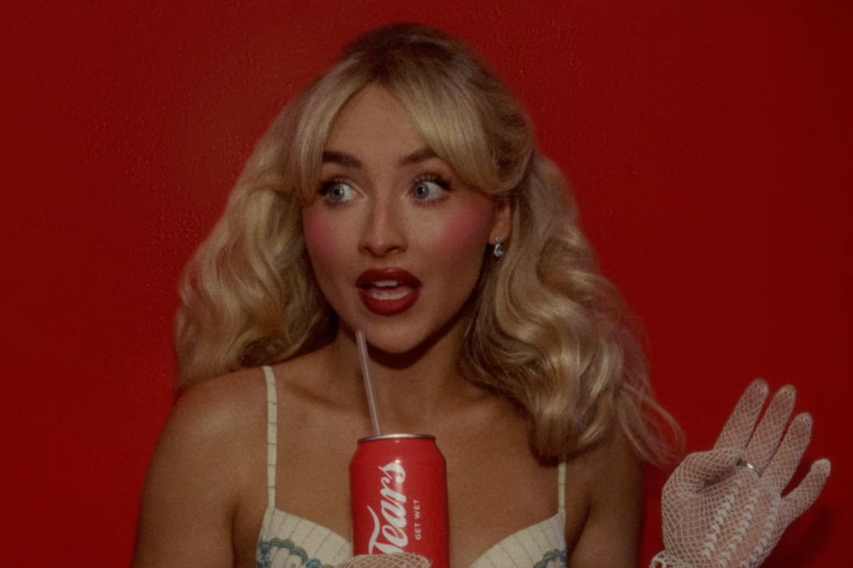 Sabrina in "Tears" music video with wavy hair, wearing a lace glove, holds a can with a straw, standing against a red background