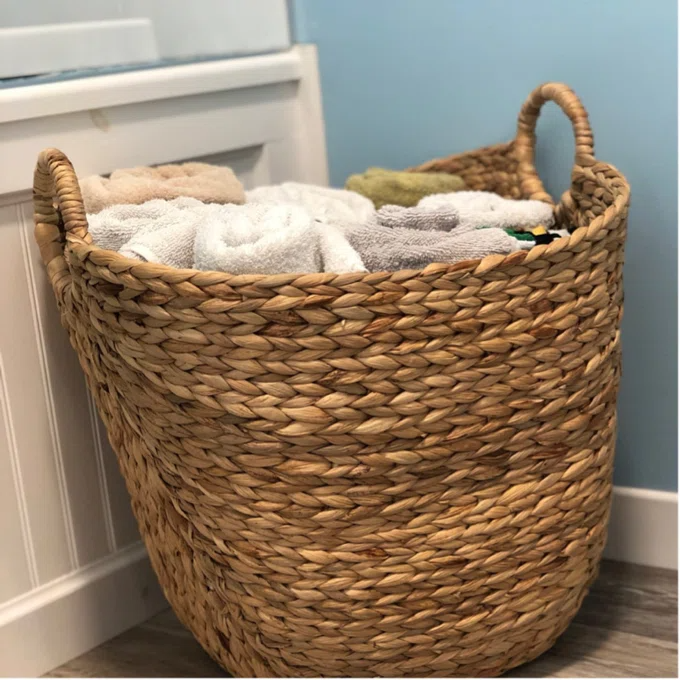 Woven basket filled with neatly folded towels, placed beside a bathroom cabinet