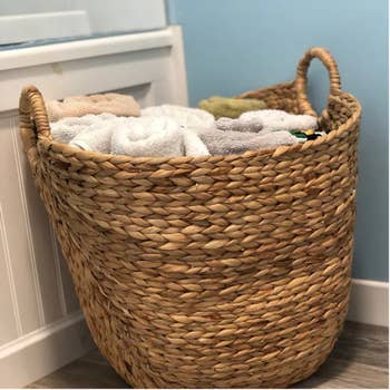 Woven basket filled with neatly folded towels, placed beside a bathroom cabinet
