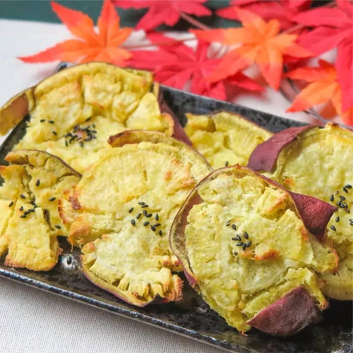 焼き芋チップスが黒い皿に盛られており、後ろに紅葉が飾られています。