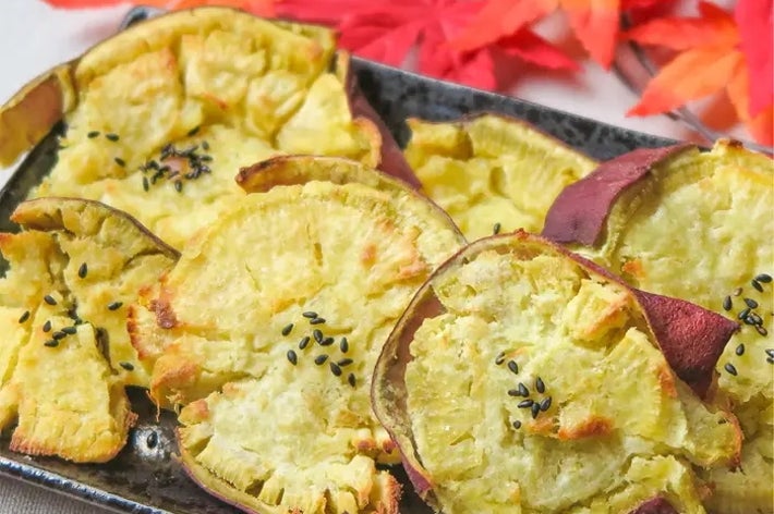 焼き芋チップスが黒い皿に盛られており、後ろに紅葉が飾られています。