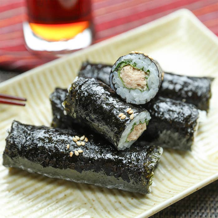 ツナと大葉ののり巻きが皿に盛られており、上に白いりごまがかかっている。後ろには飲み物が置かれている。