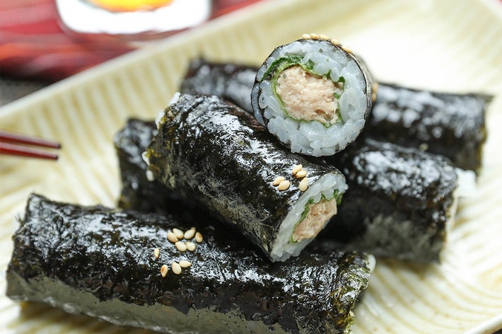 ツナと大葉ののり巻きが皿に盛られており、上に白いりごまがかかっている。後ろには飲み物が置かれている。