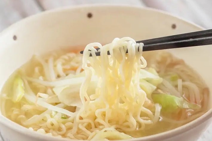 箸で持ち上げられているラーメン。ボウルにはスープと野菜が入っている。