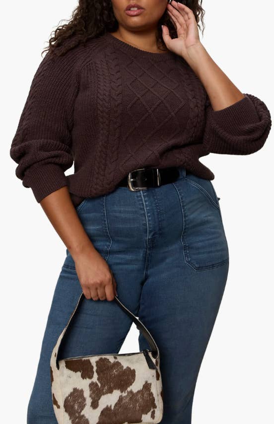Person wearing a textured sweater and high-waisted jeans, holding a stylish cowhide-patterned bag