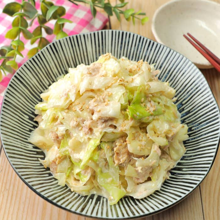 キャベツとツナのサラダが皿に盛られている。ごまがトッピングされている。背景に箸と植物が少し見える。