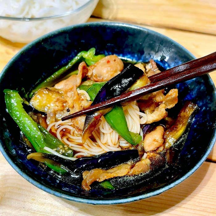 麺の上にナスと肉が盛られた料理が器に入っている。横に箸が置かれている。
