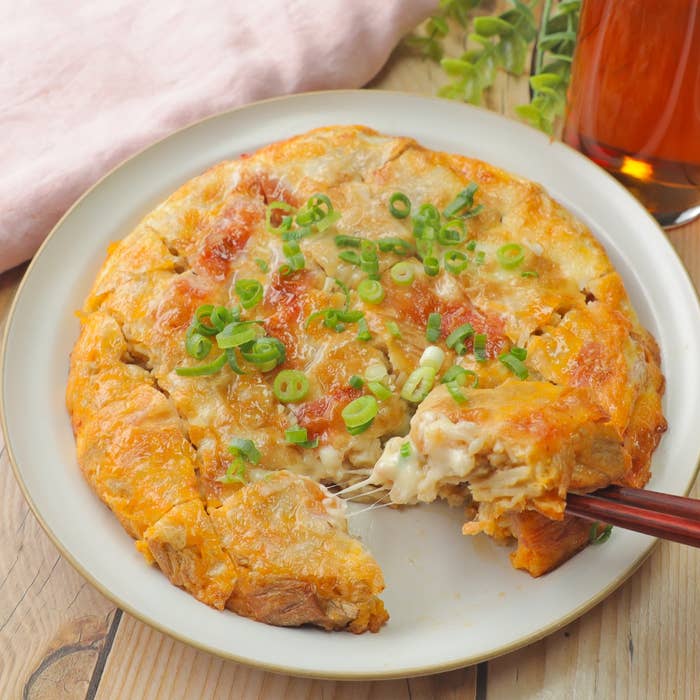料理が皿に盛られ、青ネギがトッピングされている。片隅から一部が食べられている。隣に飲み物がある。