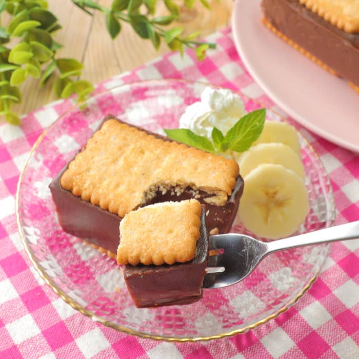 ビスケットでデコレーションされたチョコレートケーキがフォークに乗っている。隣にバナナのスライスがある。