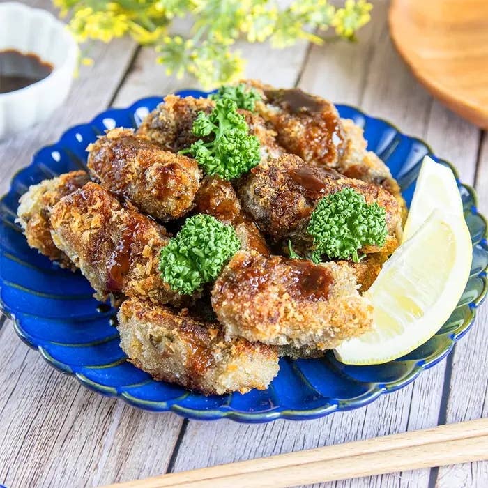 レモンとパセリが添えられた、青い皿に乗った揚げ物。背景にソースと花が見える。