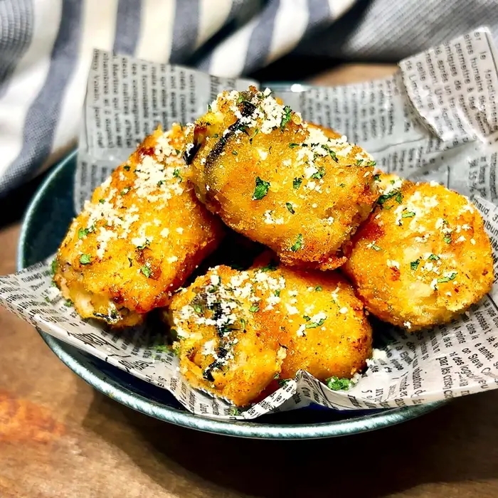 皿に盛られた揚げたなす料理。新聞紙が敷かれている。パセリとチーズが振りかけられている。
