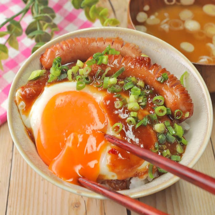 おいしそうな目玉焼きとソーセージがご飯の上にのり、青ネギが散らされている料理。箸でつままれている。
